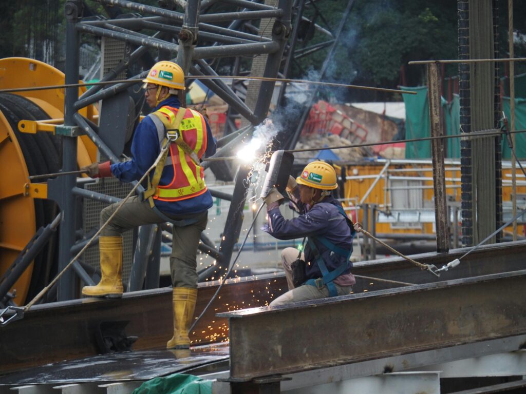 Construction workers welding metal on a bustling Hong Kong site, capturing urban development.